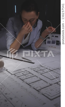 Architect woman experiencing stress and frustration from project deadline working late at night in office. Architecture and business concept in low key lighting Architect woman experiencing stress and frustration from project deadline working late at night in office. Architecture and business concept in low key lighting 138237541