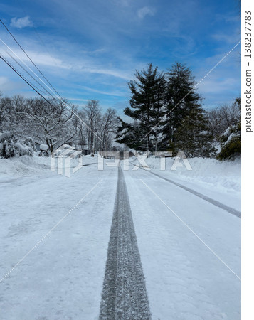 Blue sky and tire tracks stretching across a snow-covered residential street. Blue sky and tire tracks stretching across a snow-covered residential street. 138237783