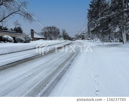 A winter scene of a snow-covered, winding road in a residential area and an icy surface. A winter scene of a snow-covered, winding road in a residential area and an icy surface. 138237785