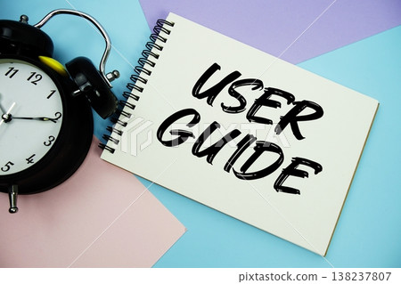 User Guide text written on notepad with alarm clock flat lay on multicolor pastel background 138237807