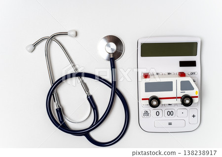 A model of an ambulance placed on top of a stethoscope and calculator illustrates the concept of medical costs. A model of an ambulance placed on top of a stethoscope and calculator illustrates the concept of medical costs. 138238917