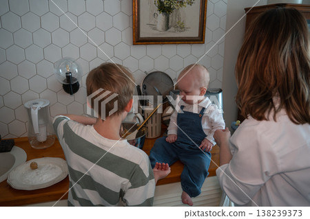 Family baking together in kitchen, mother and children preparing dough while baby sits on countertop. Home cooking, parenting, family bonding, domestic lifestyle, everyday family Family baking together in kitchen, mother and children preparing dough while baby sits on countertop. Home cooking, parenting, family bonding, domestic lifestyle, everyday family 138239373