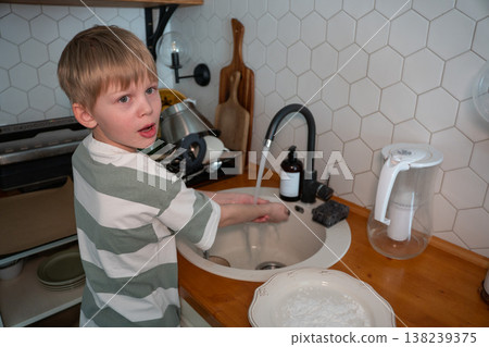 Child washes hands at kitchen sink during home baking preparation, everyday family cooking routine. Learning hygiene, child involvement, domestic lifestyle, home Child washes hands at kitchen sink during home baking preparation, everyday family cooking routine. Learning hygiene, child involvement, domestic lifestyle, home 138239375