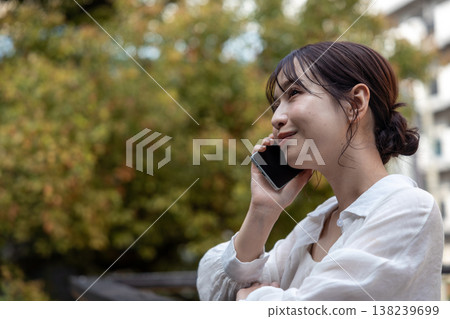 A young woman talking on her cell phone in an outdoor area with trees. 138239699