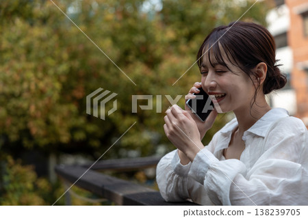 A young woman talking on her cell phone in an outdoor area with trees. A young woman talking on her cell phone in an outdoor area with trees. 138239705