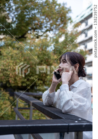 A young woman talking on her cell phone in an outdoor area with trees. A young woman talking on her cell phone in an outdoor area with trees. 138239752