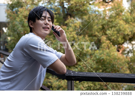 A young man talking on his cell phone in a treey area. 138239888