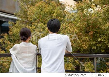 The backs of a young man and woman standing close together on a balcony. 138240776