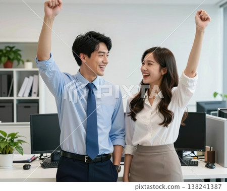 Excited Asian business couple raising fists in victory celebration at modern office. 138241387