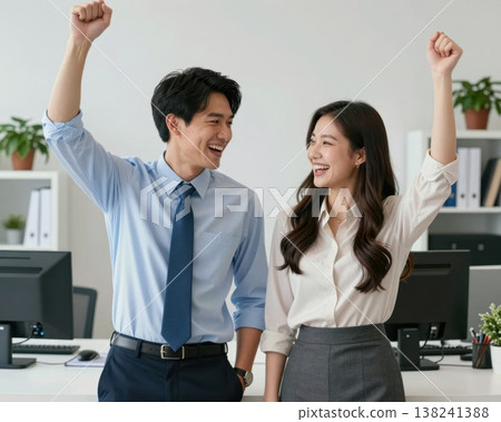 Excited Asian business couple raising fists in victory celebration at modern office. 138241388