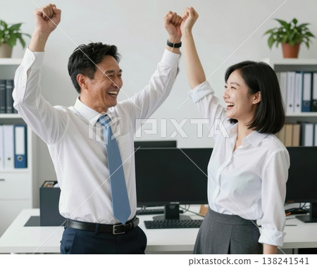 Excited Asian business couple raising fists in victory celebration at modern office. 138241541