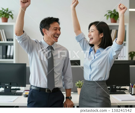 Excited Asian business couple raising fists in victory celebration at modern office. 138241542