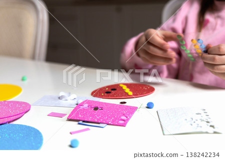 Child hands making festive easter egg craft with glue and foam shapes. 138242234