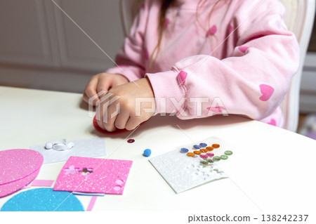 Child hands making festive easter egg craft with glue and foam shapes. 138242237
