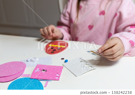 Child hands making festive easter egg craft with glue and foam shapes. 138242238