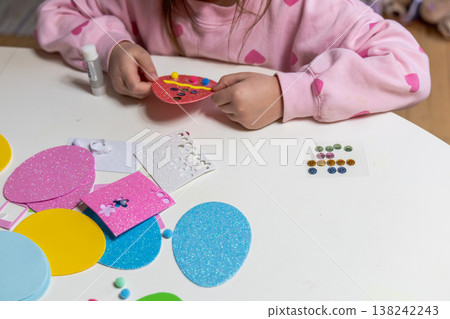 Child hands making festive easter egg craft with glue and foam shapes. Child hands making festive easter egg craft with glue and foam shapes. 138242243
