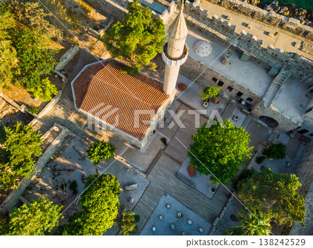 Aerial view of a historic seaside citadel featuring a stone minaret and crenelated walls in golden sunlight. 138242529