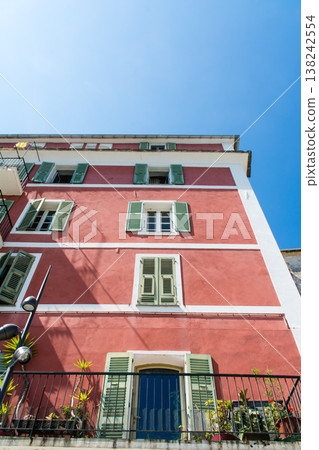 A pale red pastel-colored building with blackout doors, bathed in bright sunlight, on the French island of Corsica in the Mediterranean Sea. 138242554