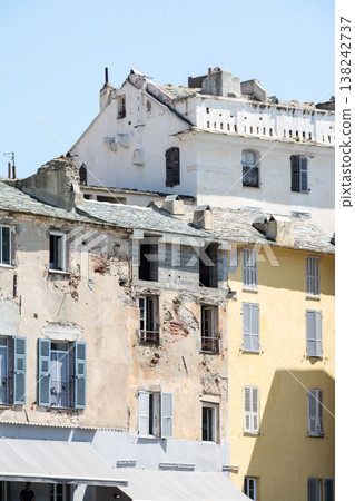 A pastel-colored building with blackout doors bathed in bright sunlight on the French island of Corsica in the Mediterranean Sea. 138242737