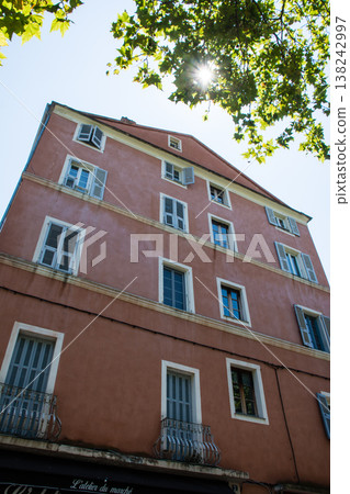 A pale red pastel-colored building with blackout doors, bathed in bright sunlight, on the French island of Corsica in the Mediterranean Sea. A pale red pastel-colored building with blackout doors, bathed in bright sunlight, on the French island of Corsica in the Mediterranean Sea. 138242997