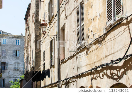 A pastel-colored building with blackout doors bathed in bright sunlight on the French island of Corsica in the Mediterranean Sea. 138243031