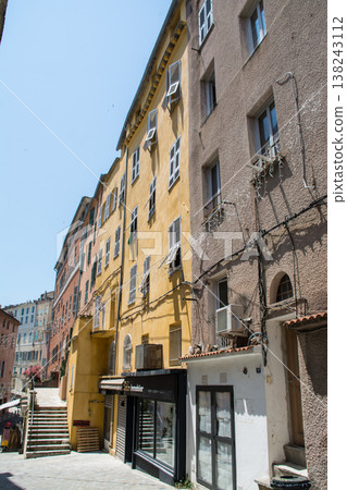 A pastel-colored building with blackout doors bathed in bright sunlight on the French island of Corsica in the Mediterranean Sea. 138243112