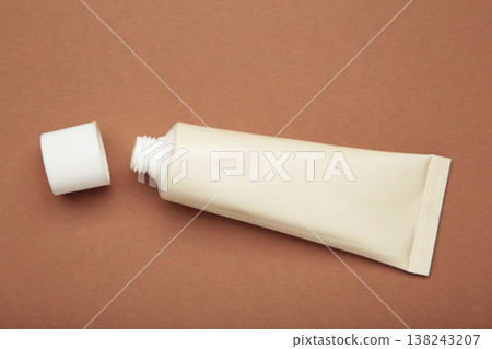 Beige tube of cream on brown background. Mockup plastic tube for cosmetics Beige tube of cream on brown background. Mockup plastic tube for cosmetics 138243207