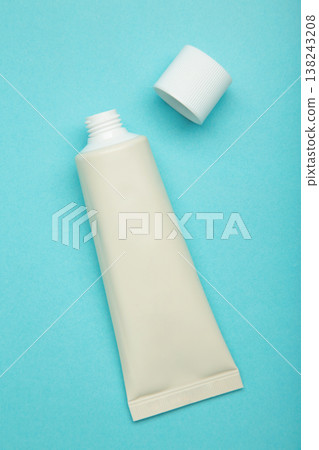 Beige tube of cream on blue background. Mockup plastic tube for cosmetics. Vertical photo Beige tube of cream on blue background. Mockup plastic tube for cosmetics. Vertical photo 138243208