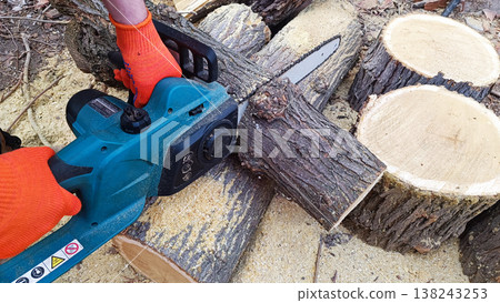 Hand holds chain saw with battery to trim broken branch of an tree. Modern work with electric portable brushless cordless chain saw. Hand holds chain saw with battery to trim broken branch of an tree. Modern work with electric portable brushless cordless chain saw. 138243253