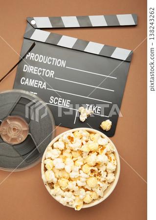 Movie clapper with popcorn and film reels on brown background Movie clapper with popcorn and film reels on brown background 138243262