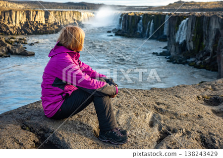 Witness the majesty of Selfoss waterfall in Iceland, as a visitor enjoys the scenic views along the riverbank surrounded by nature Witness the majesty of Selfoss waterfall in Iceland, as a visitor enjoys the scenic views along the riverbank surrounded by nature 138243429
