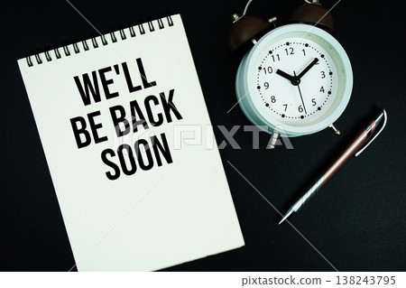 We'll Be Back Soon text written on notepad with pen and alarm clock 138243795
