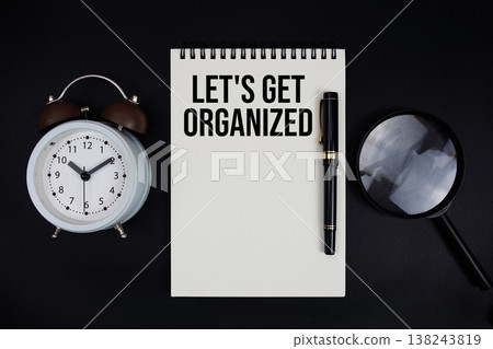 Let's Get Organized text written on notepad with alarm clock top view on black background Let's Get Organized text written on notepad with alarm clock top view on black background 138243819