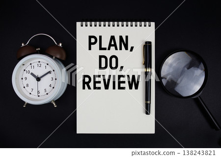 Plan, Do, Review text written on notepad with alarm clock top view on black background Plan, Do, Review text written on notepad with alarm clock top view on black background 138243821
