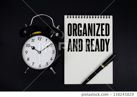 Organized And Ready text written on notepad with alarm clock top view on black background Organized And Ready text written on notepad with alarm clock top view on black background 138243829