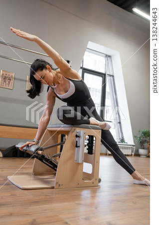 Woman doing side plank pilates variation on wooden box in sleek fitness studio. Side plank, pilates, wooden box, studio, workout. Woman doing side plank pilates variation on wooden box in sleek fitness studio. Side plank, pilates, wooden box, studio, workout. 138244643