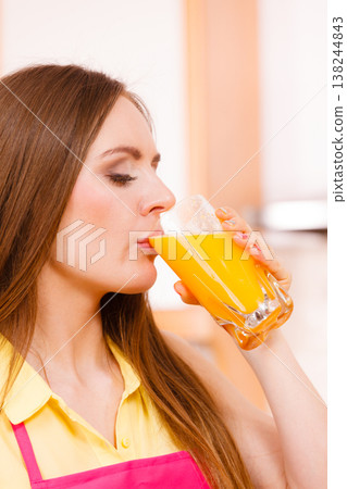 Woman in kitchen drinking fresh orange juice 138244843