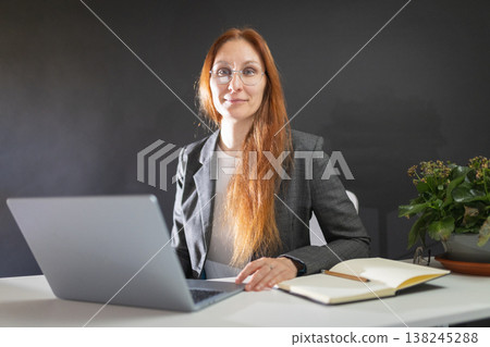 Woman working on laptop while smiling at camera 138245288