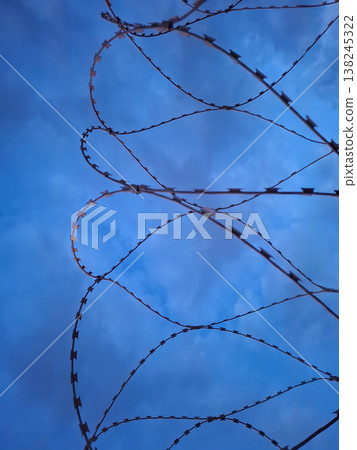 Barbed wire is seen against a gloomy sky. The scene represents limitation and confinement, evoking feelings of restriction and loss of freedom. The atmosphere feels heavy and tense. Barbed wire is seen against a gloomy sky. The scene represents limitation and confinement, evoking feelings of restriction and loss of freedom. The atmosphere feels heavy and tense. 138245322