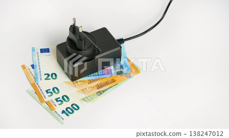 Black power adapter resting on euro banknotes, symbolizing increasing electricity costs and the energy crisis impacting household budgets Black power adapter resting on euro banknotes, symbolizing increasing electricity costs and the energy crisis impacting household budgets 138247012