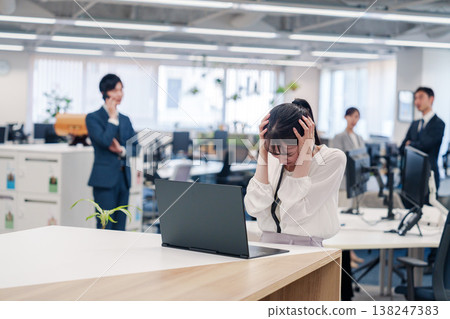A woman holding her head in her hands in the office A woman holding her head in her hands in the office 138247383