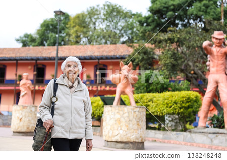 Happy senior lifestyle concept. Senior woman at the central square of the beautiful small town of Raquira. The city of pots in Colombia. Happy senior lifestyle concept. Senior woman at the central square of the beautiful small town of Raquira. The city of pots in Colombia. 138248248