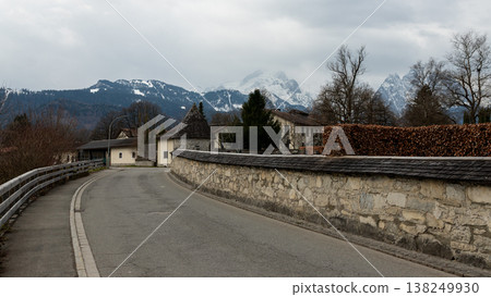 Curved village road with stone wall and snowy alpine mountains in Bavaria Curved village road with stone wall and snowy alpine mountains in Bavaria 138249930