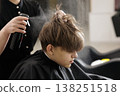 Hairdresser applies styling spray while cutting a boys hair in a barbershop. Hair care, grooming routine, salon service, and hygiene concept. 138251518