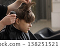 Hairdresser sprays styling product on a boy hair while cutting in a barbershop. Grooming, hair care routine, hygiene, and salon service concept. 138251521