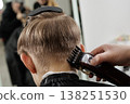Hairdresser uses an electric clipper to trim the nape area of a boy hair in a barbershop. Close-up of haircut process, grooming service, hygiene, and care concept. 138251530