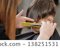 Hairdresser trims a boy bangs using scissors and a comb. Close-up of haircut process, grooming routine, and hairstyling service in salon. 138251531