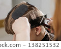 Hairdresser uses clipper over comb technique to trim hair in a barbershop. Close-up of haircut process, grooming service, hygiene, and precision styling concept. 138251532