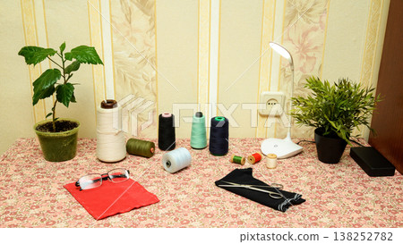set of thread spools on table with scissors and glasses near desk lamp in home sewing studio workspace set of thread spools on table with scissors and glasses near desk lamp in home sewing studio workspace 138252782