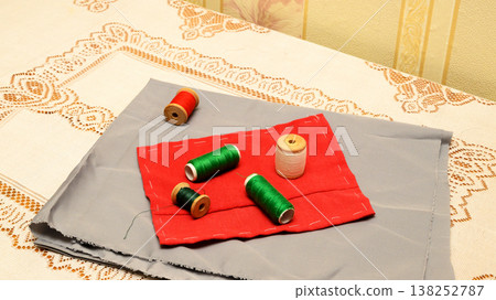 detailed view of spools of thread on patches of gray and red fabric on a lace table detailed view of spools of thread on patches of gray and red fabric on a lace table 138252787